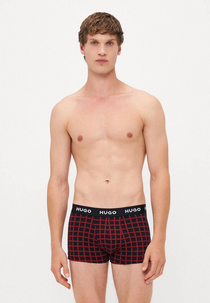 Boxer-briefs à carreaux noirs et rouges avec une large taille noire affichant "HUGO" en lettres blanches. Tissu lisse, coupe ajustée.