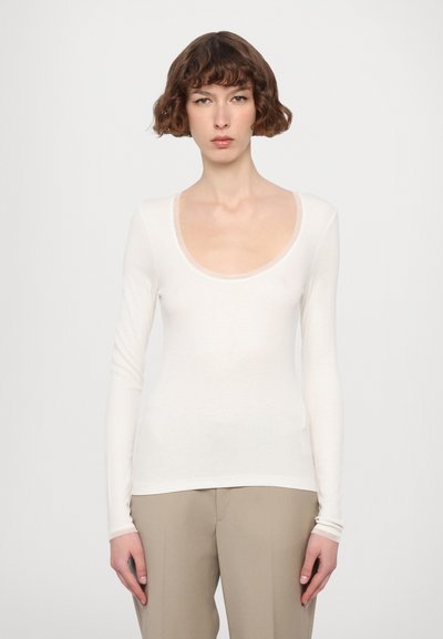 Langærmet bluse med scoop-neck i let, off-white materiale med en tætsiddende silhuet og ribbet tekstur. Sammen med beige bukser.