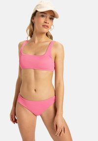 Pink ribbed bikini with a square neckline and wide straps. The bottom features a classic cut. Includes a light-colored cap.