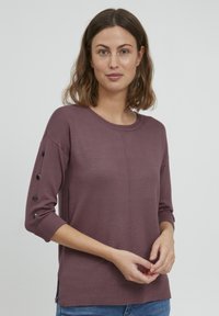 Bordó könnyű pulóver háromnegyedes ujjakkal, gombdíszekkel az ujjakon, kerek nyakkivágással és oldalsó hasítékokkal az alján.