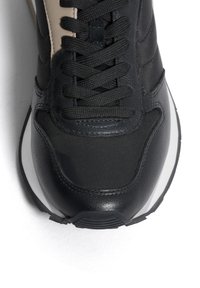 Sneaker nera caratterizzata da un mix di materiali in pelle e tessuto, punta tonda, lacci piatti e suola esterna bianca a contrasto.