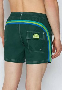 Costumi da bagno verdi con strisce laterali blu e gialle, vita elastica, tasca posteriore con patta e patch con il logo. Tessuto intrecciato, taglio corto.