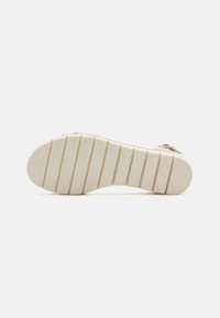 Beiger Sandalenboden mit einem strukturierten Design, horizontalen Rillen und abgerundeten Akzenten, aus Gummi für Haltbarkeit und Traktion gefertigt.