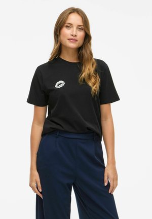 T-shirt en coton noir avec un imprimé de lèvres argenté sur la poitrine gauche, associé à un pantalon bleu marine. Coupe décontractée et manches courtes.