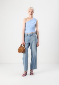 Top azul claro de un solo hombro, jeans de tiro alto azul claro, tacones morados con tiras y un pequeño bolso marrón texturizado.