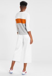 Sweter robiony na drutach w białe, pomarańczowe i szare poziome paski; zestawiony z białymi spodniami w szerokim kroju i czerwono-białymi butami sportowymi.