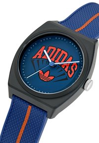 Montre Adidas avec un cadran rond bleu et un logo rouge, un boîtier noir, et un bracelet en silicone texturé bleu avec une bande d'accent orange.