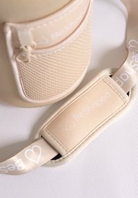 Sac BeShaped en matériau beige doux avec une poche zippée et une bandoulière réglable arborant un logo. Texture lisse avec un subtil détail en maille.