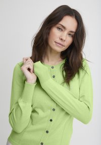 Cardigan verde a maglia con collo rotondo, chiusura con bottoni e polsini a coste. Presenta bottoni neri e un design aderente.