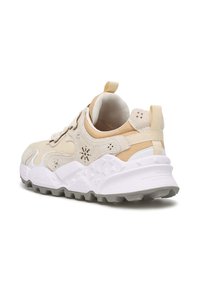 Beige Sneaker mit einer strukturierten Oberseite, durchbrochenen Akzenten und einer weißen Zwischensohle mit einem robusten Profilmuster auf der grauen Außensohle.