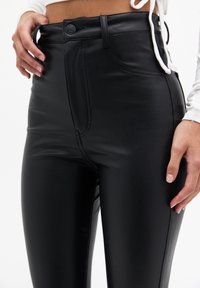 Zwarte faux leren high-waisted broek met een soepele textuur, sluiting met knoop aan de voorkant en zijzakken, met zichtbare stiksels.
