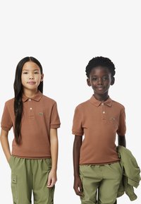 Polo marroni a maniche corte, con un piccolo logo Lacoste verde. Abbinati a pantaloni cargo verdi, che mostrano un look informale.