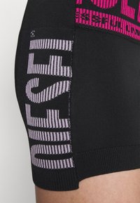 Zwarte gebreide shorts met opvallende roze en paarse letters. Het ontwerp bevat gestreepte patronen en een naadloze afwerking langs de randen.