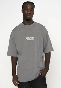 Szara, oversize'owa koszulka z miękkiego materiału z białym logo "MULTIPLY APPAREL" na lewej piersi i krótkimi rękawami.