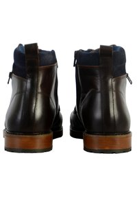 Botas de cuero marrón a la altura del tobillo con forro textil en color navy, cremalleras laterales y tacones de madera. Acabado de cuero suave con texturas contrastantes en el cuello.