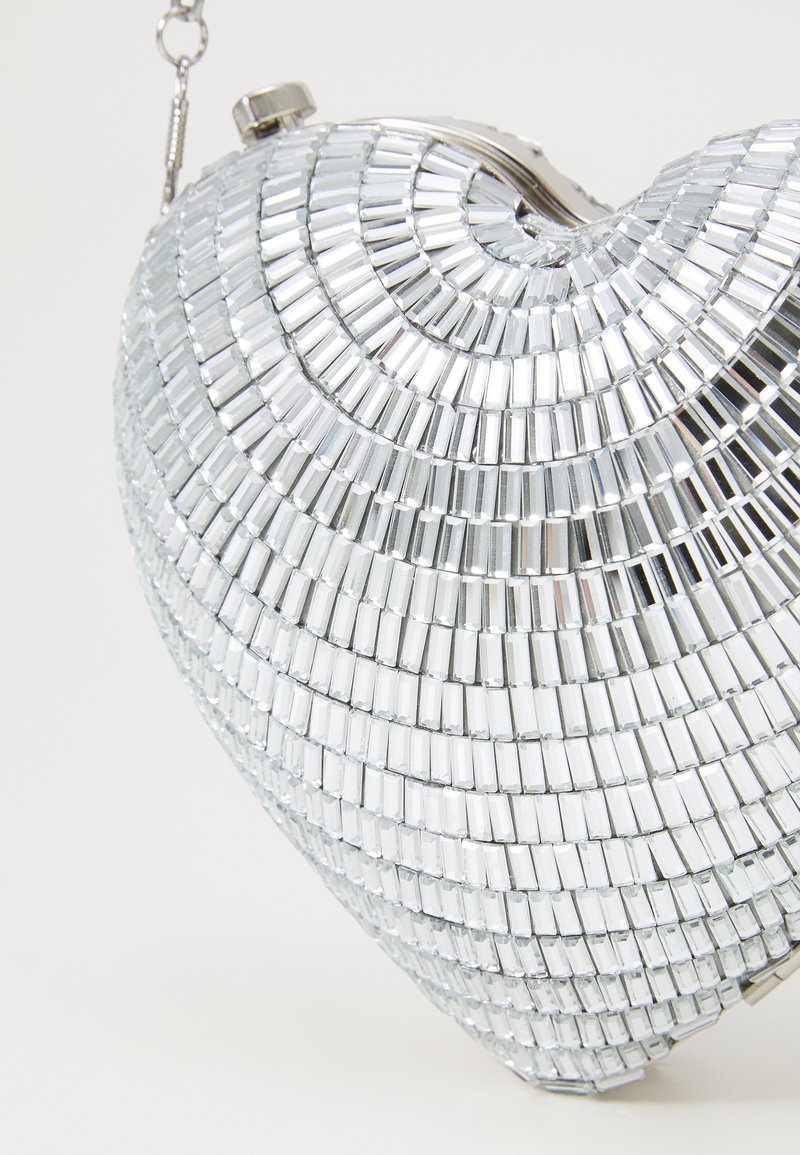 Torebka w kształcie serca wykonana z lustrzanych płytek srebrnych, z metalowym zapięciem i łańcuszkiem. Gładka tekstura z refleksyjną powierzchnią.