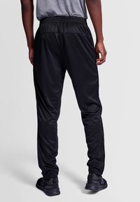 Zwarte sportbroek met een elastische tailleband en taps toelopende pijpen. Gemaakt van gladde, lichte stof. Gecombineerd met zwarte sportschoenen.