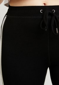 Svarta joggingsbyxor i mjukt tyg med dragsko i midjan, med ribbat mönster, silverögon och vita sidremsor.