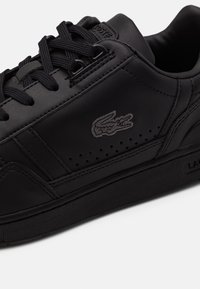 Schwarzer Ledersneaker mit schwarzen Schnürsenkeln, perforierter Seitenpartie und aufgenähtem Krokodil-Logo seitlich nahe dem gepolsterten Schaft.