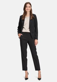 Schwarzer Anzug mit einem taillierten Blazer mit einem Knopf, Slim-Fit-Hose und einem hellbeigen Oberteil. Glatter Stoff und minimalistisches Design.