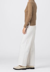 Suéter marrón de lana con puños acanalados, combinado con pantalones de mezclilla anchos blancos con dobladillos deshilachados y mocasines beige.
