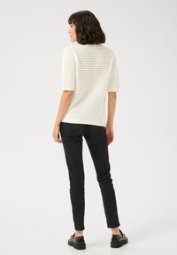 Haut court en tricot blanc à motifs en nid d'abeille, associé à un jean slim noir et des chaussures noires, vu de dos.