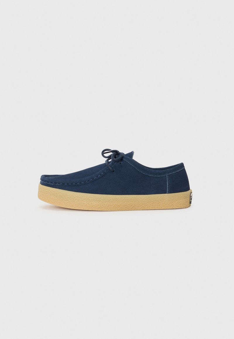 Dark blue suede shoe with round toe, lace-up design, and a tan rubber sole featuring a textured finish. Minimalistic style, no additional accents.