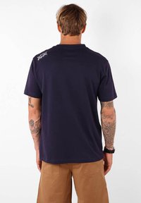 T-shirt en coton bleu marine avec une coupe décontractée. Doté d'un petit graphique sur le haut du dos et de manches courtes. Texture lisse et col rond classique.