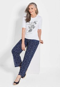 Weißes T-Shirt mit kurzen Ärmeln und schwarzem floralen Druck; marineblaue weit geschnittene Hosen mit Pünktchen; tanfarbene Espadrilles. Glatter Stoff, entspannte Passform.