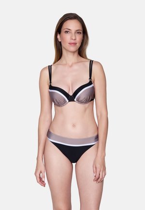 Vrouw die een tweekleurige bikini draagt met zwarte, taupekleurige en witte strepen, recht vooruitstaand tegen een effen lichte achtergrond.
