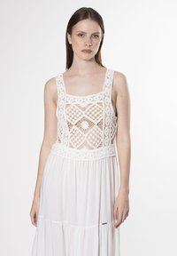 Weißes Kleid mit einem gehäkelten Oberteil, das geometrische Muster aufweist, einem quadratischen Ausschnitt und einem fließenden Rock mit einem gestuften Design.