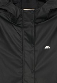Schwarze wasserfeste Jacke mit Kapuze, ausgestattet mit Druckknöpfen und einem kleinen weißen Logo auf der oberen linken Seite. Glatte Textur und minimalistisches Design.