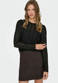 Svart blonde topp med lange ermer som har et teksturert mønster og samlet skulderdetalj, kombinert med et mørkebrunt tettsittende skjørt.