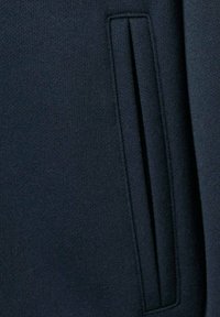 Tessuto di felpa blu navy con una texture liscia e un dettaglio discreto di tasca laterale. Caratterizzato da un design pulito e minimalista.