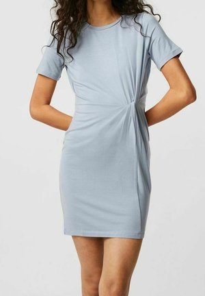 Kobieta ubrana w jasnoniebieską sukienkę z krótkim rękawem, sięgającą do kolan, z marszczonym węzłem w talii.