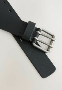 Ceinture en cuir noir avec une finition texturée et une boucle en métal argenté. La boucle dispose de plusieurs pattes, et la sangle comprend plusieurs trous de réglage.