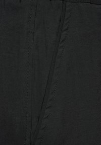 Czarna tkanina z pionowymi liniami szwów i jednym złożonym zakładką detalu na środku, pokazująca fakturę i detal szwów z bliska.