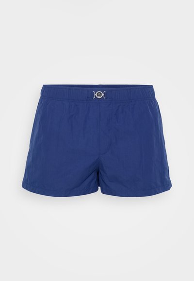 Mėlynos maudymosi šortai, pagaminti iš lengvos medžiagos, su elastinga juosta ir sidabrinėmis detalėmis priekyje. Trumpas, prigludęs dizainas.