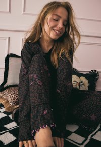 Set di pigiama nero con motivo a stampa leopardata, con accenti rosa e polsini arricciati. Tessuto morbido e vestibilità rilassata. Dettagli del motivo visibili.