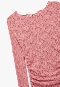 Roze kanten top met lange mouwen, voorzien van een textuur met bloemmotieven en een geplooid detail aan de zijkant. Ronde halslijn, zachte stof.