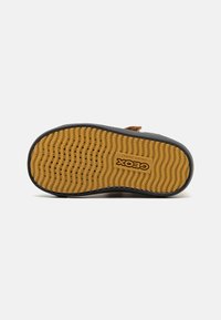 Suela de zapato marrón para niño con agarre texturizado amarillo, pequeñas perforaciones para transpirabilidad y el logo "GEOX Patente Italiana".