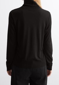 Schwarzer Rollkragenpullover mit langen Ärmeln, aus einem glatten Stoff gefertigt. Verfügt über eine enganliegende Passform am Kragen und am Bund.