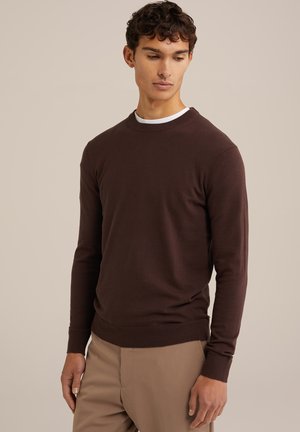 Brown knitted sweater with a crew neck, ribbed cuffs and hem, made of soft fabric. Worn over a white T-shirt, featuring a fitted design.