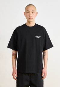 Crna pamučna majica kratkih rukava, okrugli izrez i bijeli vezeni "Carhartt" logo na lijevoj strani prsnog koša. Jednostavan, ležeran kroj.