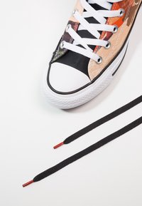 Vysoké tenisky s oranžovou, černou a béžovou plátěnou vrstvou, bílé gumové špičky a černé tkaničky, se červeně zakončenými konci tkaniček.