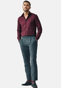 Cămașă bordo cu mâneci lungi, asociată cu pantaloni gri plisati și pantofi de birou negri. Cămașa are o textură netedă; pantalonii sunt adaptați.