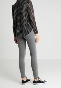 Black polka dot long-sleeve shirt, gray skinny jeans, and black canvas sneakers with white soles. Smooth fabric; fitted silhouette.