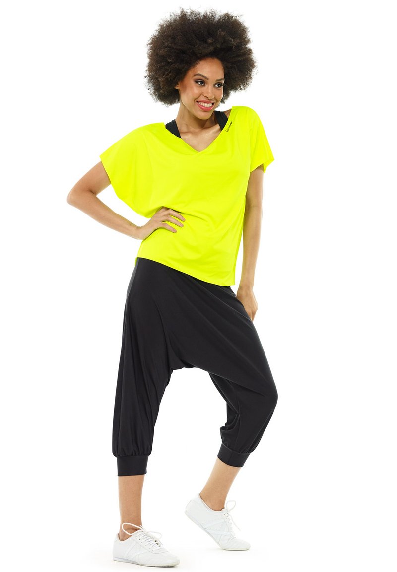 Yellow oversized short-sleeve top paired with loose black harem pants and white sneakers. The fabric appears soft and lightweight.