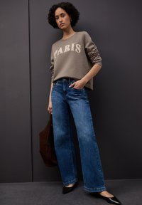 Szara bluza z napisem "PARIS", zestawiona z niebieskimi dżinsami z wysokim stanem i szerokimi nogawkami. Całość uzupełniają czarne szpiczaste baleriny oraz brązowa torebka.