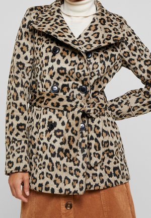 Leopardprintet frakke med bælte og dobbeltradede sorte knapper, bæres over en hvid rullekrave og en brun manchesterskørt.